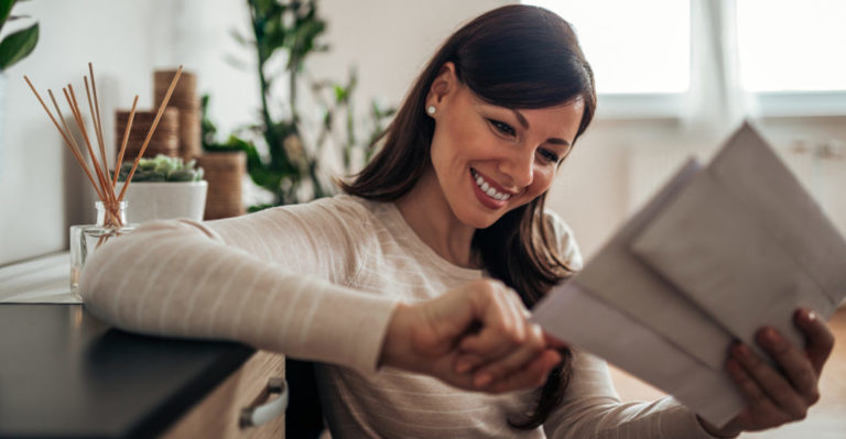 Smiling woman looking at received mail at home, close-up.